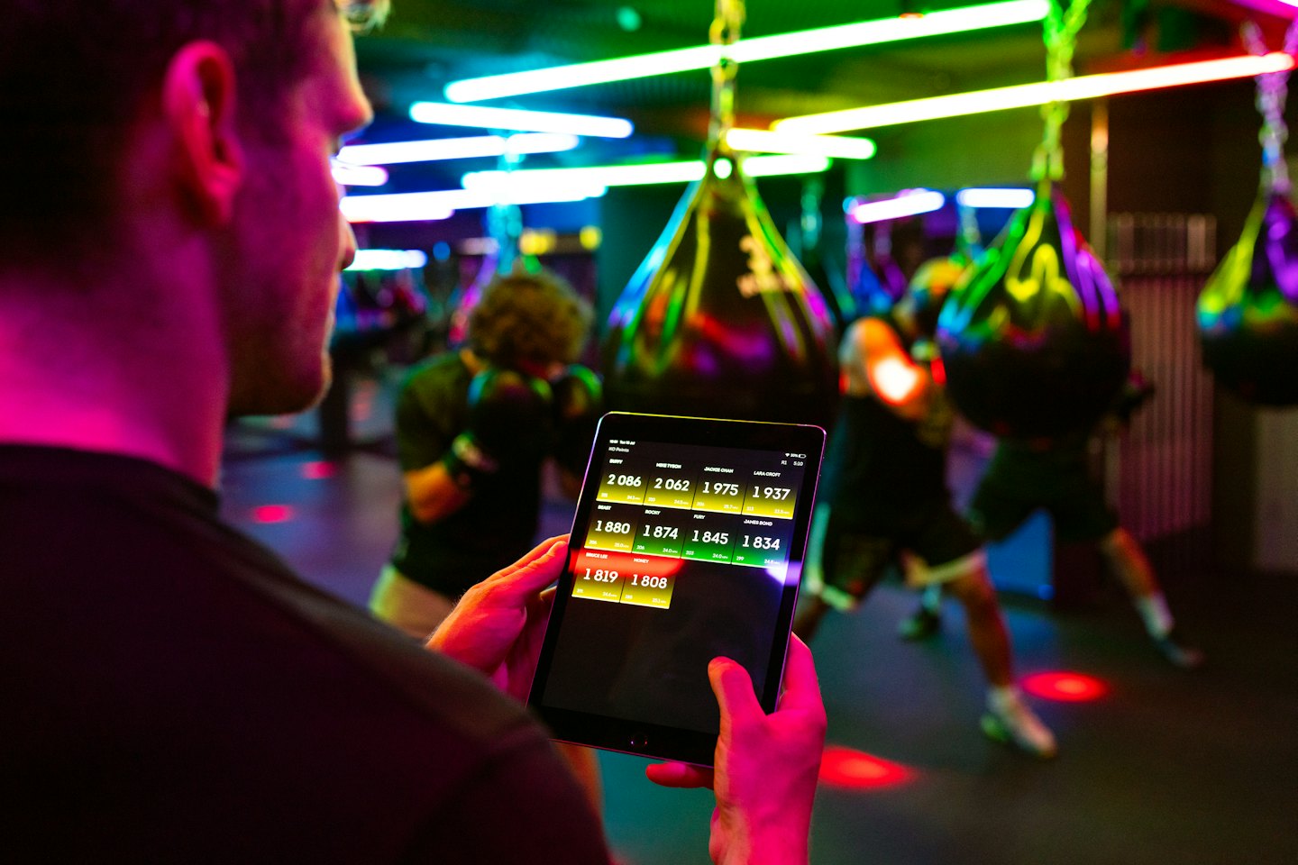 Man reviews fitness data on tablet in a neon-lit gym.