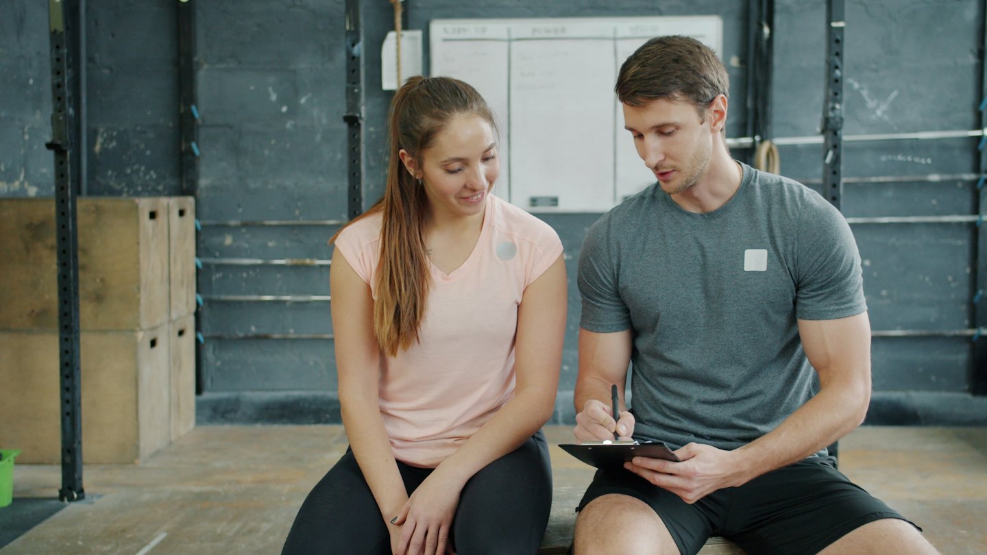 Personal trainer writes notes on a clipboard for a client.